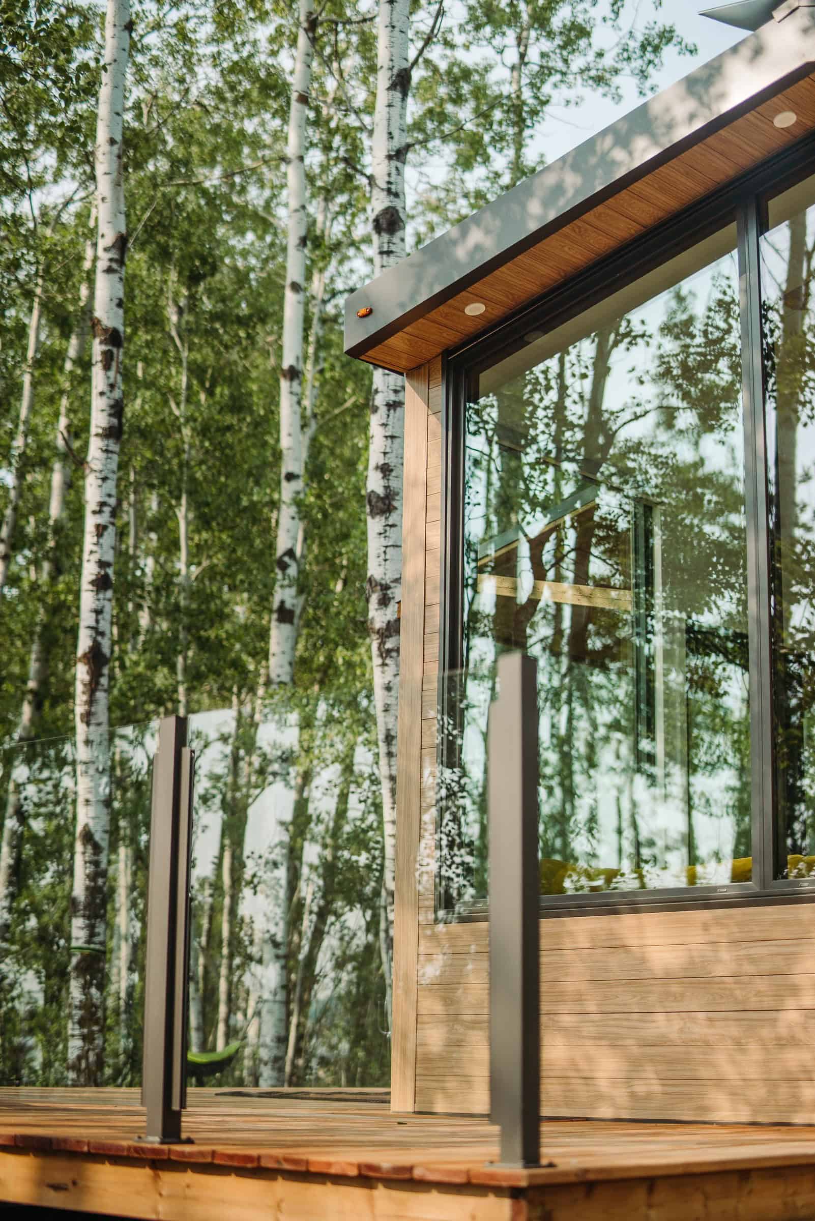 Fritz Halcyon 01 in birch: light wood siding, floor-to-ceiling glass, glass-rail wood deck, soffit lights, Devon Alberta