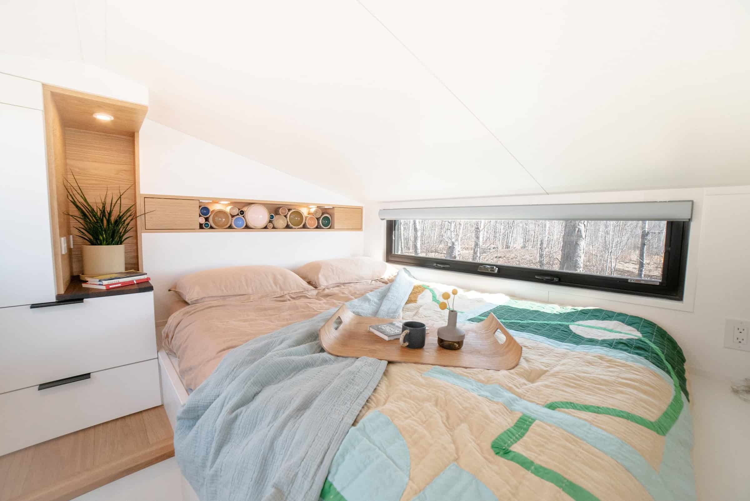 Halcyon 01 standing loft: bed with a geometric quilt, wardrobe and drawer built-ins, lit headboard niche, window to the trees