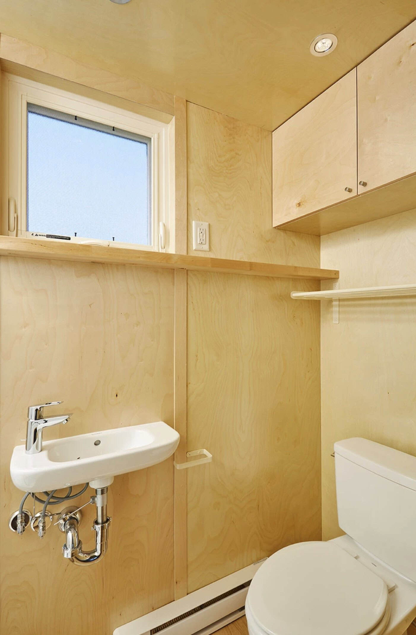 Birch bathroom with a wall-mounted sink under a frosted operable window, a Toto toilet, and storage cabinets with silver knobs