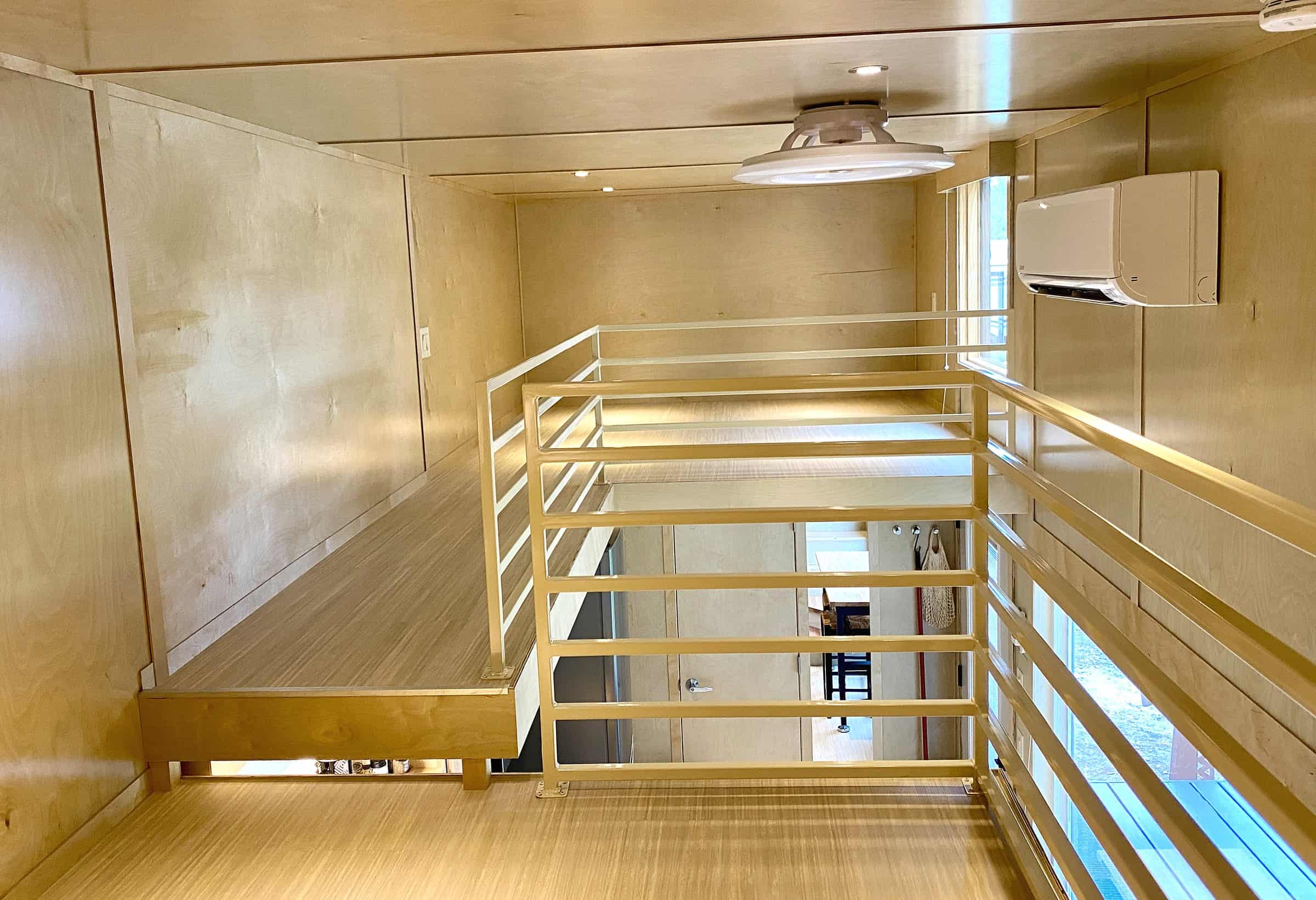 Upper level of the eONE: two birch loft platforms connected by a railed walkway, white horizontal railings, recessed lights, and a mini-split on the wall