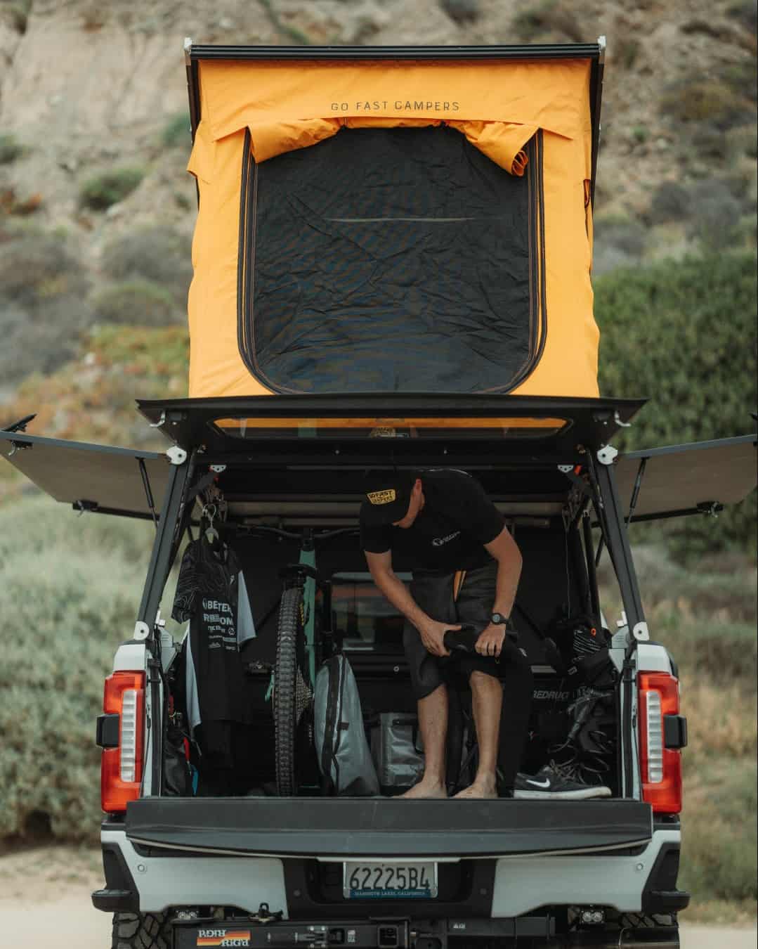 Go Fast Campers V2 Pro with side and rear panels open for truck-bed access under the orange wedge