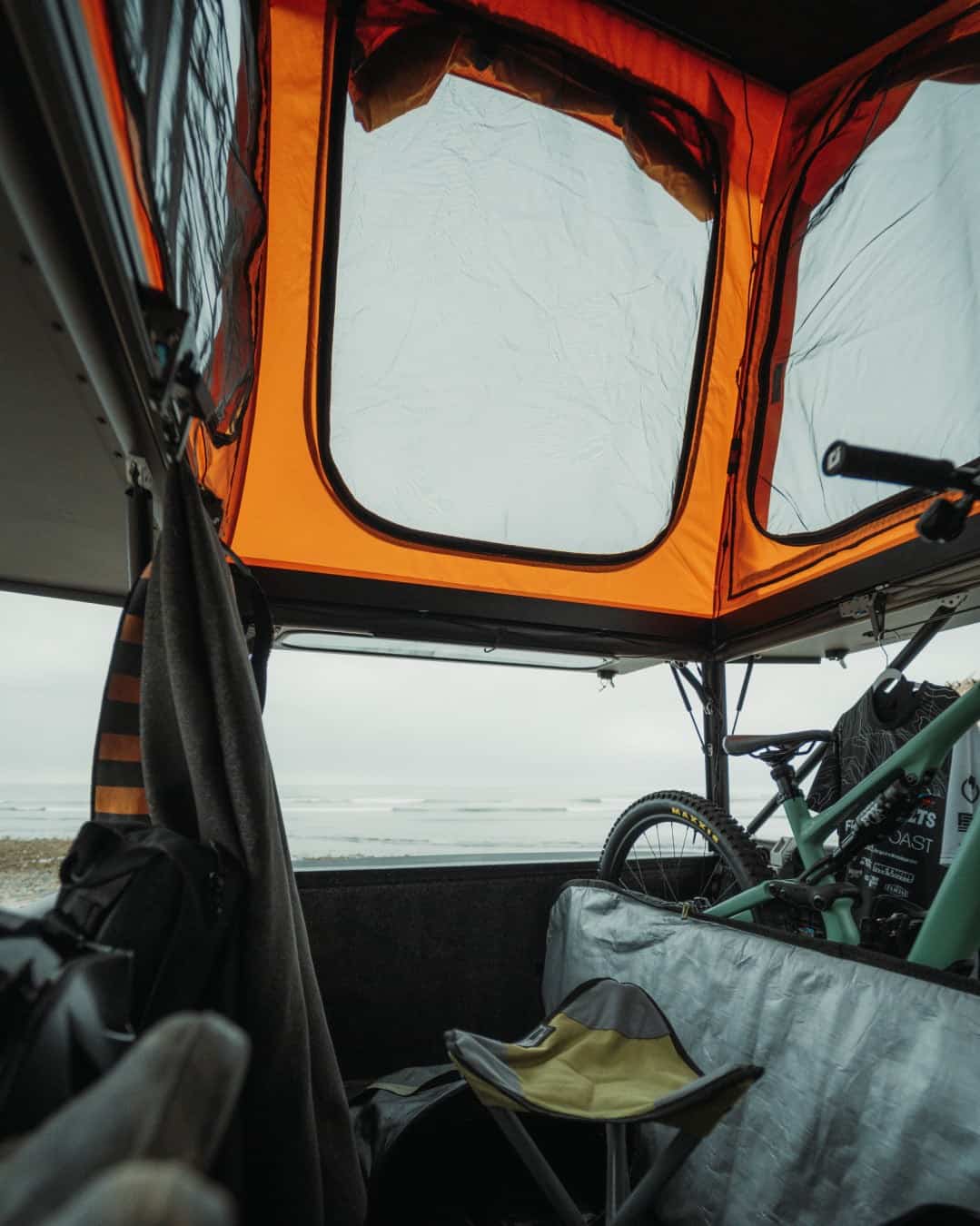 Interior view through Go Fast Campers V2 Pro mesh windows toward the ocean with bike stowed in bed