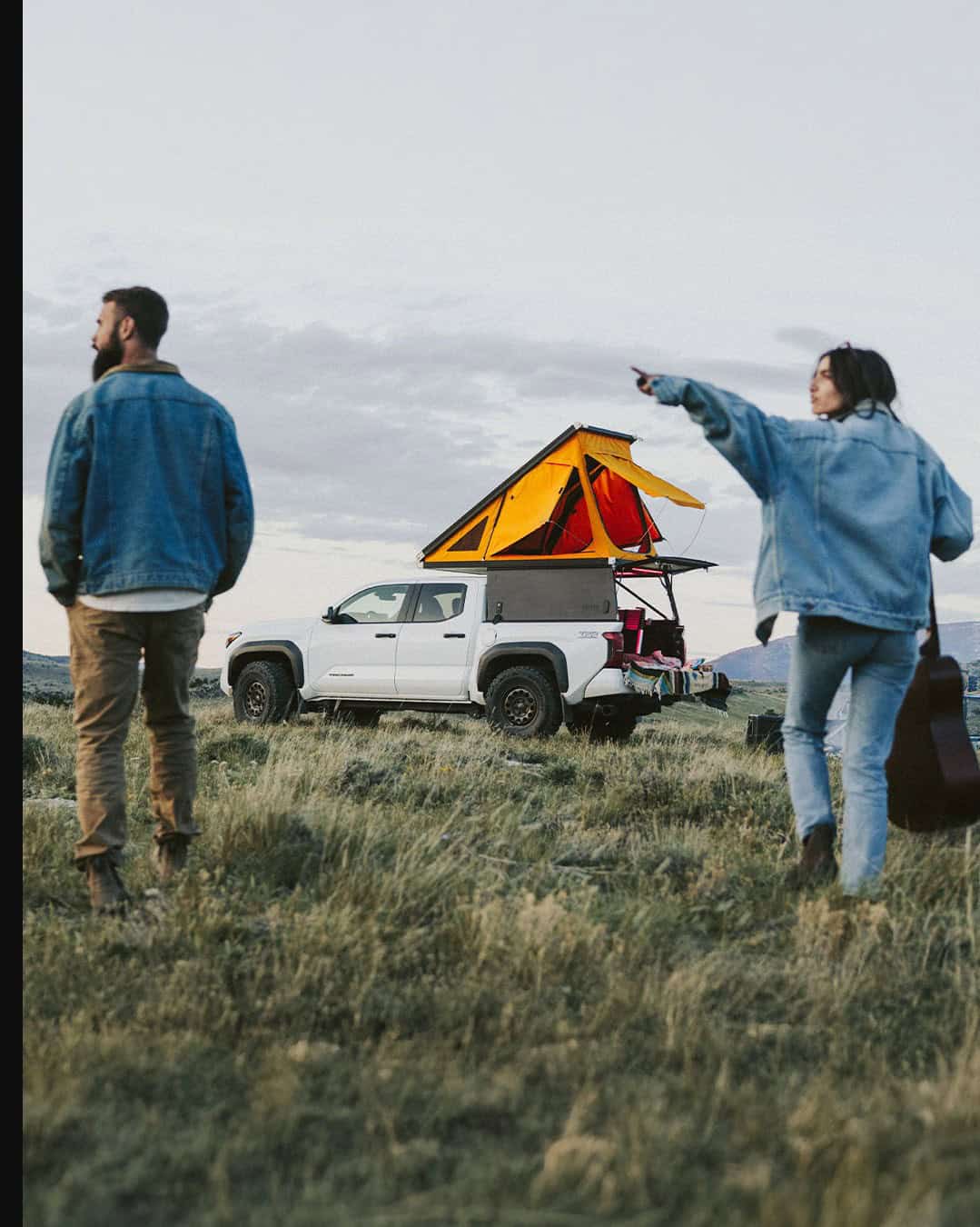 Go Fast Campers V2 Pro with orange wedge tent open on a white pickup in a grassy field at dusk