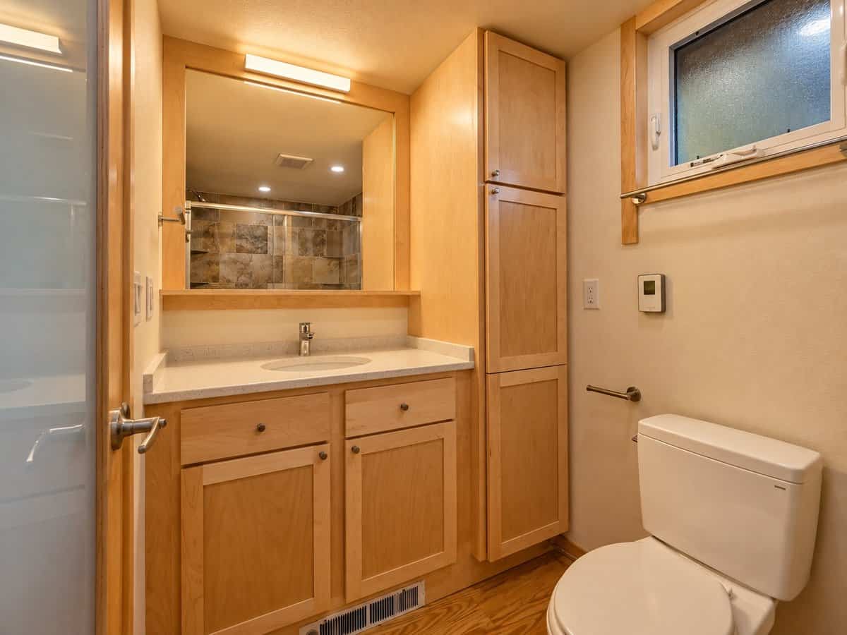 Spacious bathroom with a maple vanity, quartz counter, large mirror and full-height linen cabinet in the GLASS HOUSE Lot 25
