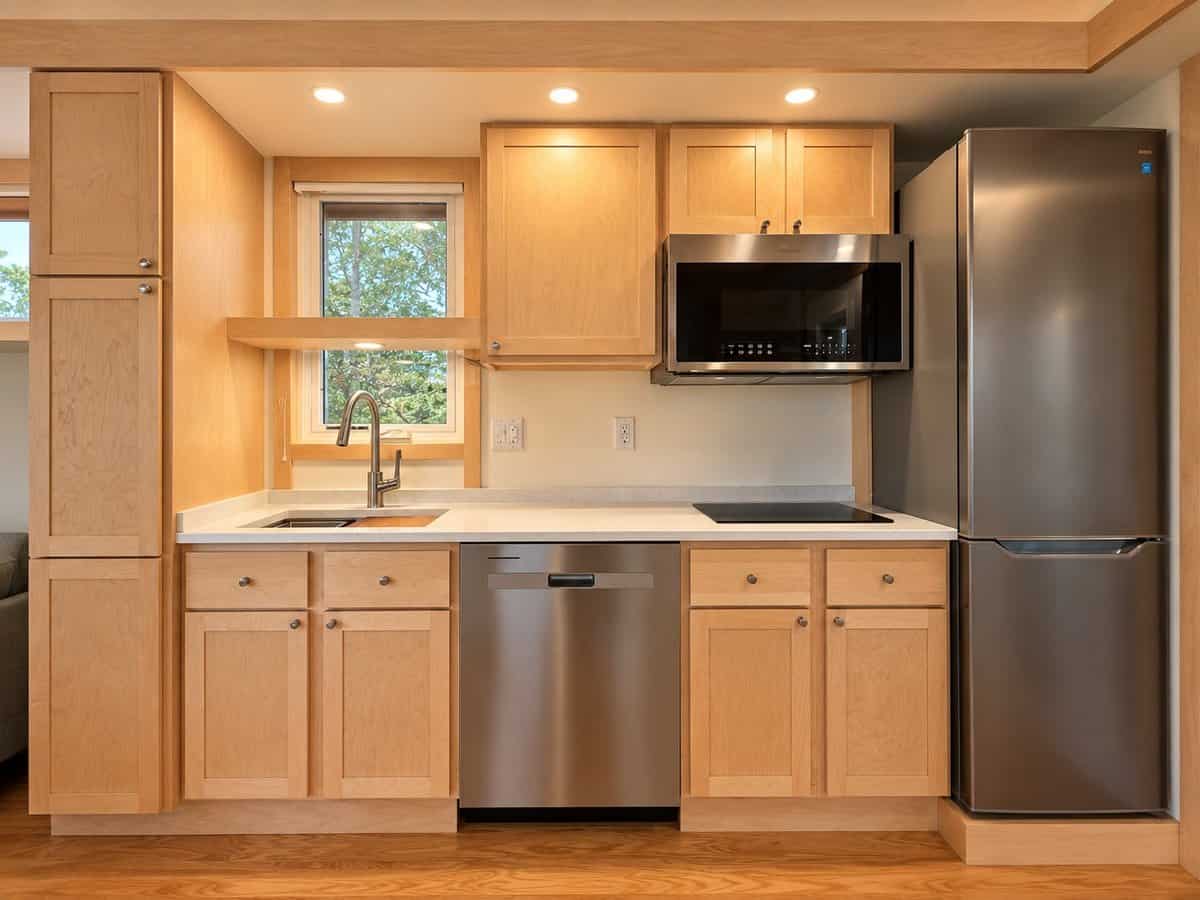 Modern kitchen with maple shaker cabinets, quartz countertops, induction cooktop, stainless dishwasher, microwave and full-height refrigerator in the GLASS HOUSE Lot 25