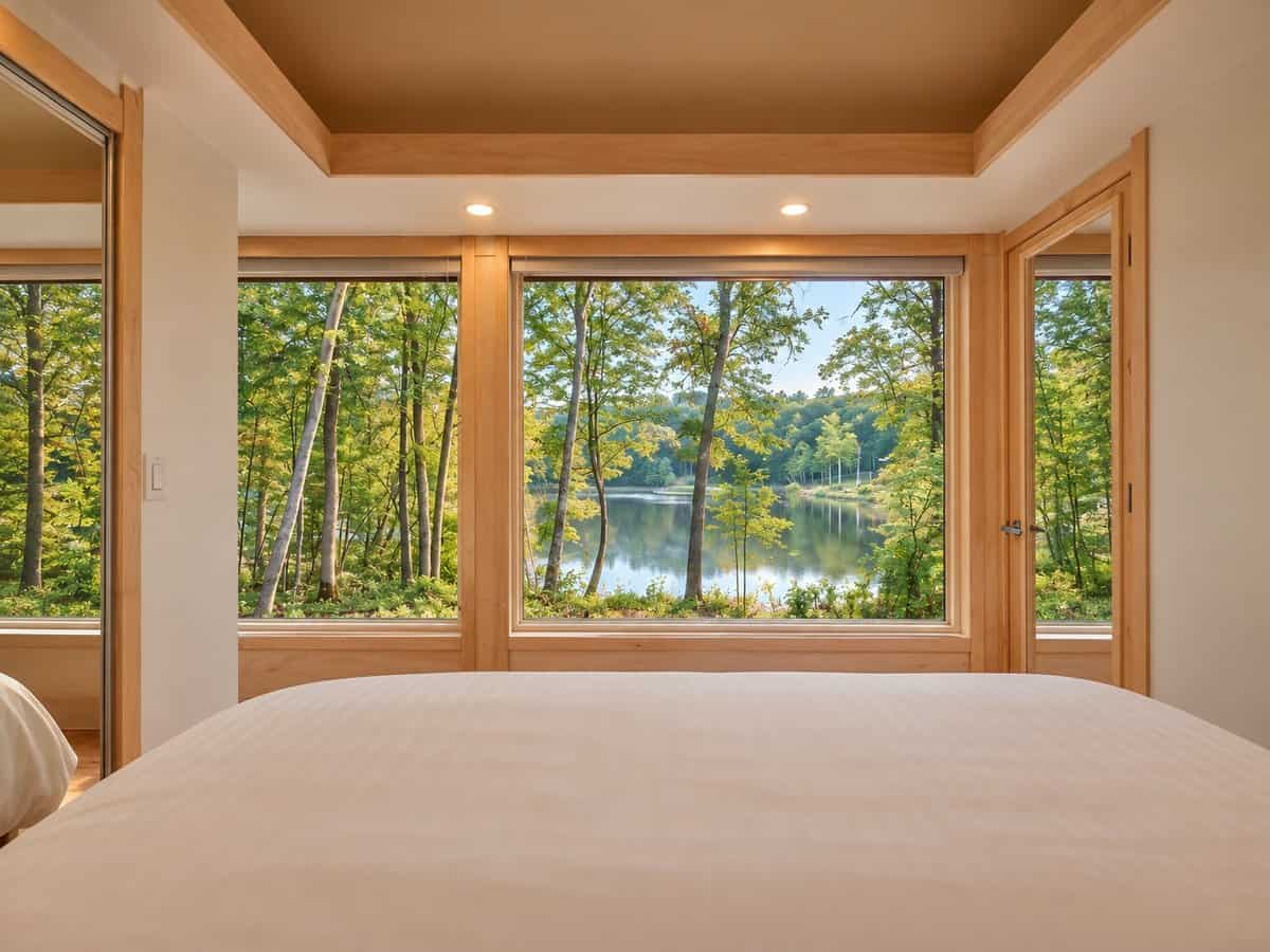 View of Lost Lake through floor-to-ceiling corner windows from the foot of the king bed in the GLASS HOUSE Lot 25