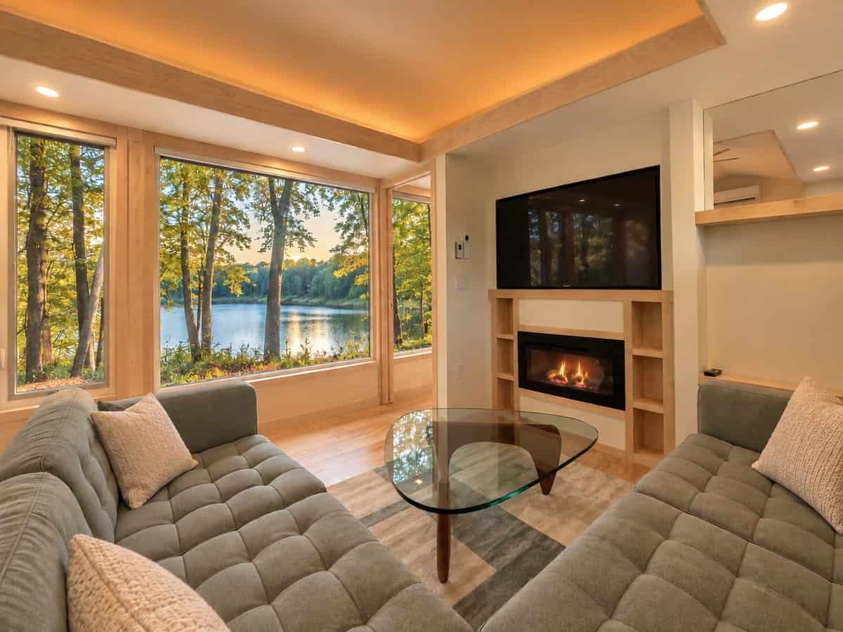Sectional seating around a glass coffee table facing a built-in fireplace with an oversized Smart TV above it in the GLASS HOUSE Lot 25