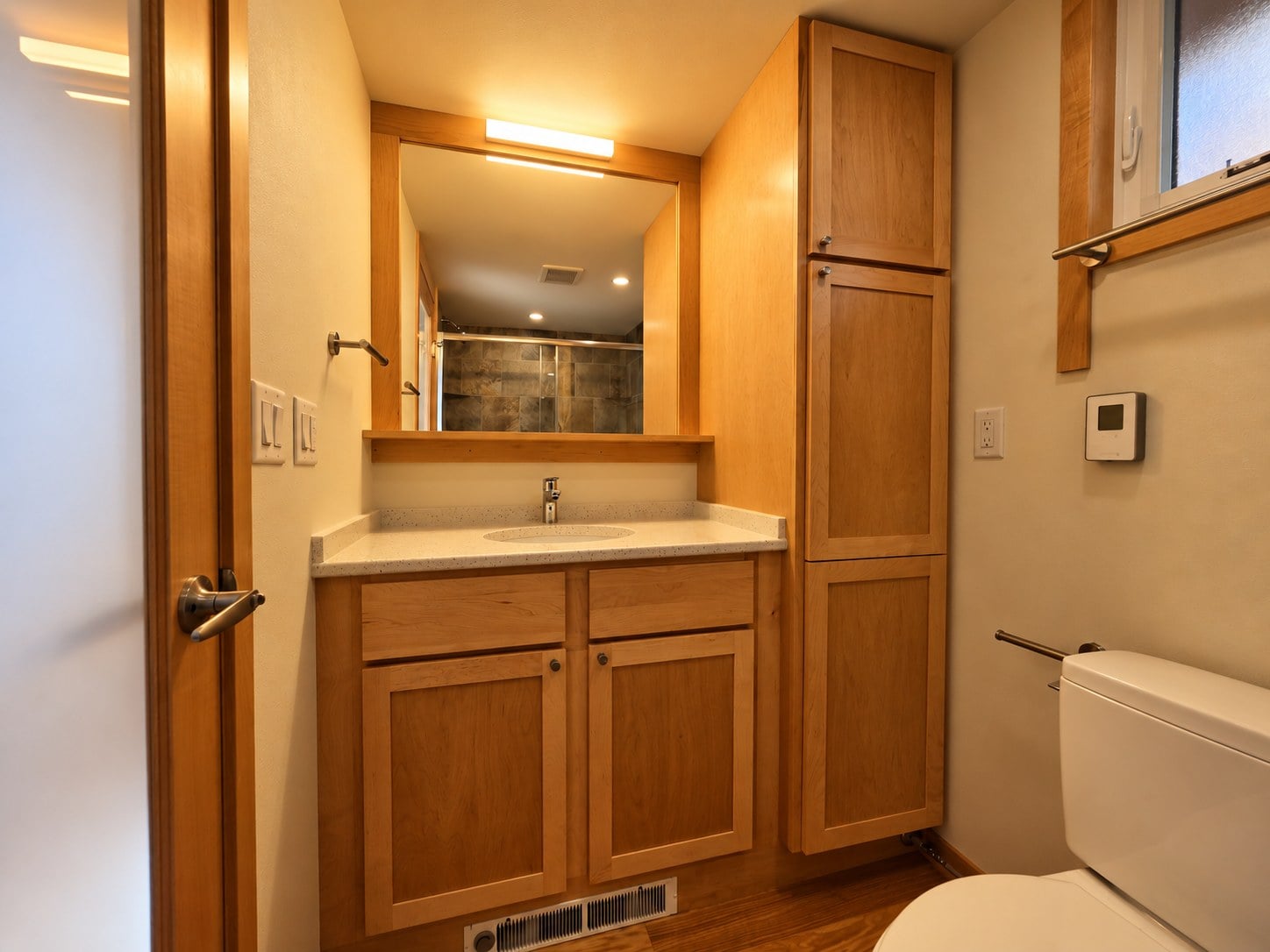 Bathroom in the Glass House Lot 27 with a maple vanity, large mirror and full-height storage cabinet