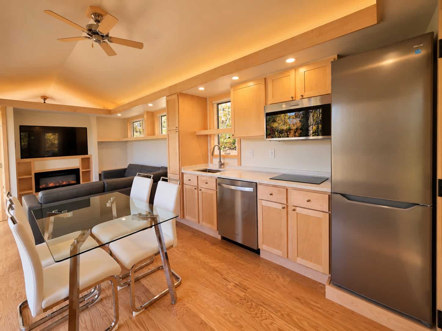 Kitchen and great room in the Glass House Lot 27 with maple cabinets, dishwasher, tall refrigerator, glass dining table, sectional and fireplace