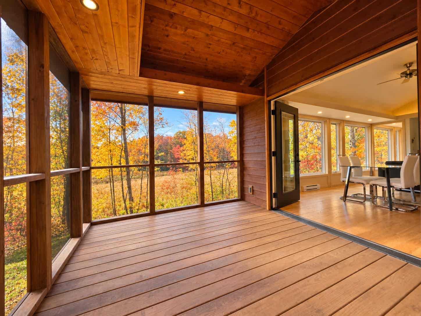 Cedar-lined screened porch of the Glass House Lot 27 with an open glass door into the great room and fall wetland views
