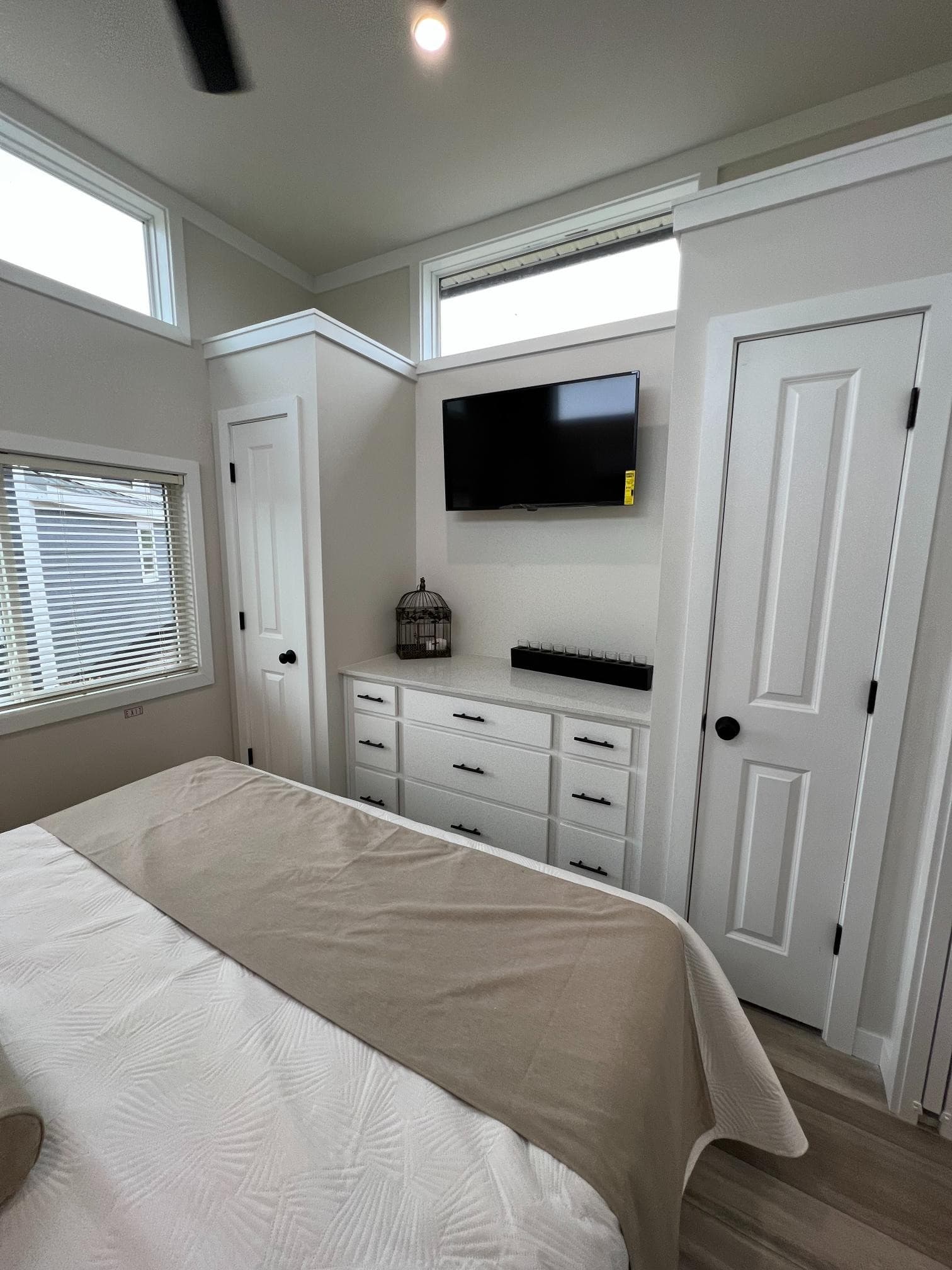 Bayview 300 bedroom opposite wall: white nine-drawer dresser, wall TV, flanking closet doors, clerestory windows