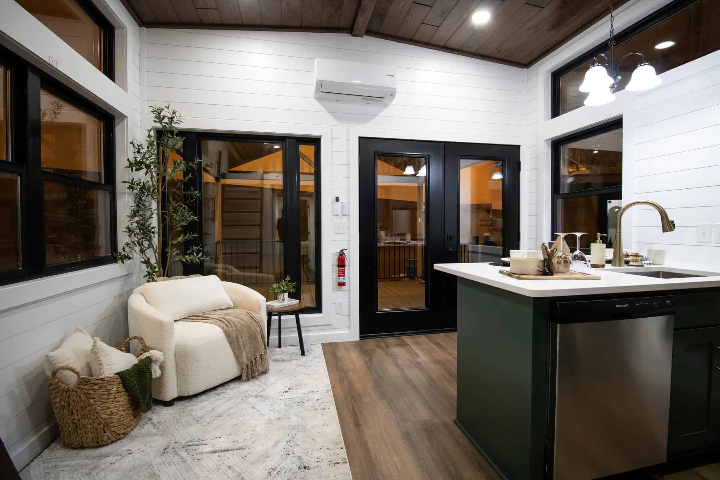 Living corner of A-Frame Luxe: white armchair, green island with dishwasher, black-framed French doors, Bosch wall unit