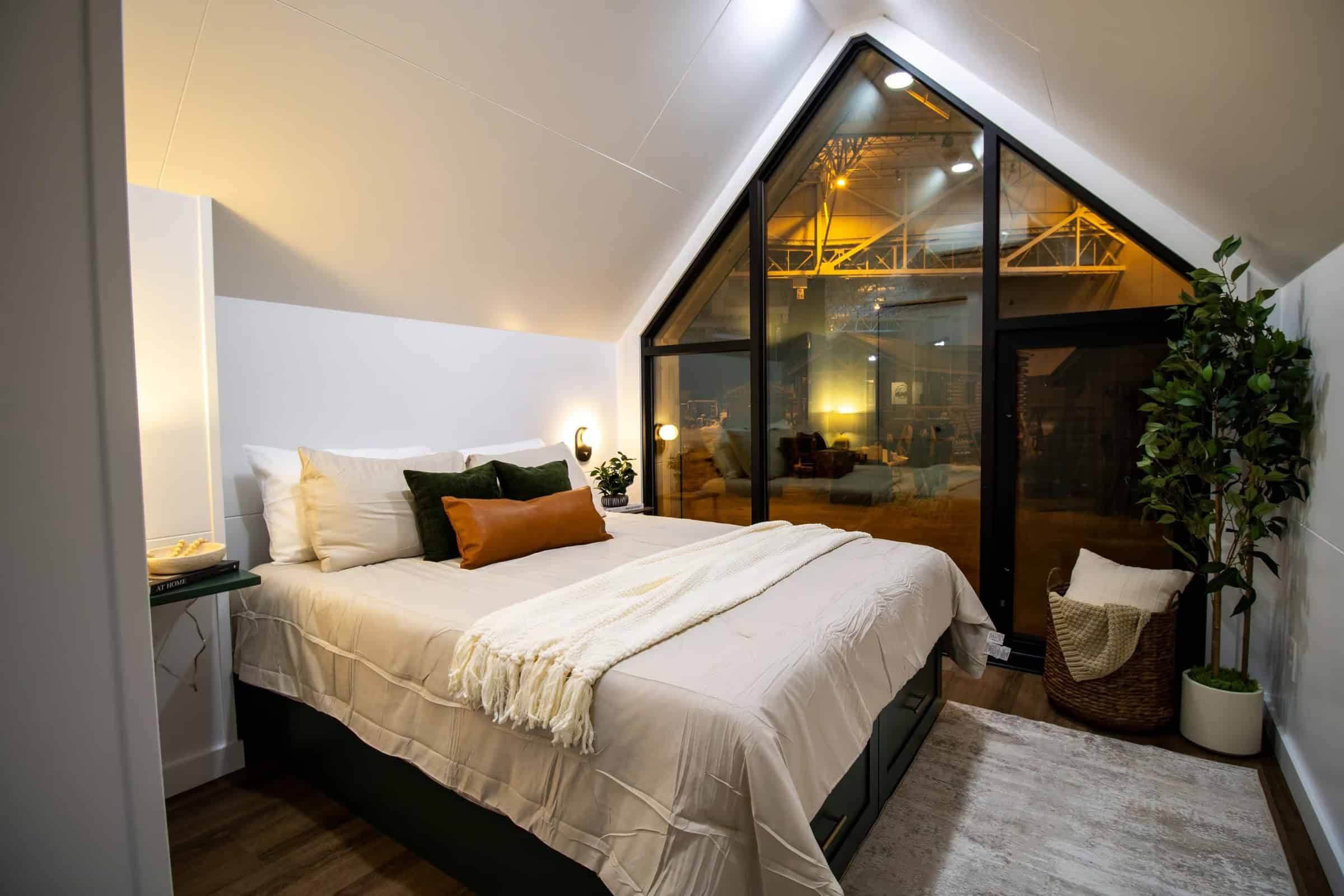 Main-floor bedroom: green platform bed, vaulted white ceiling, floor-to-ceiling triangular black-framed window