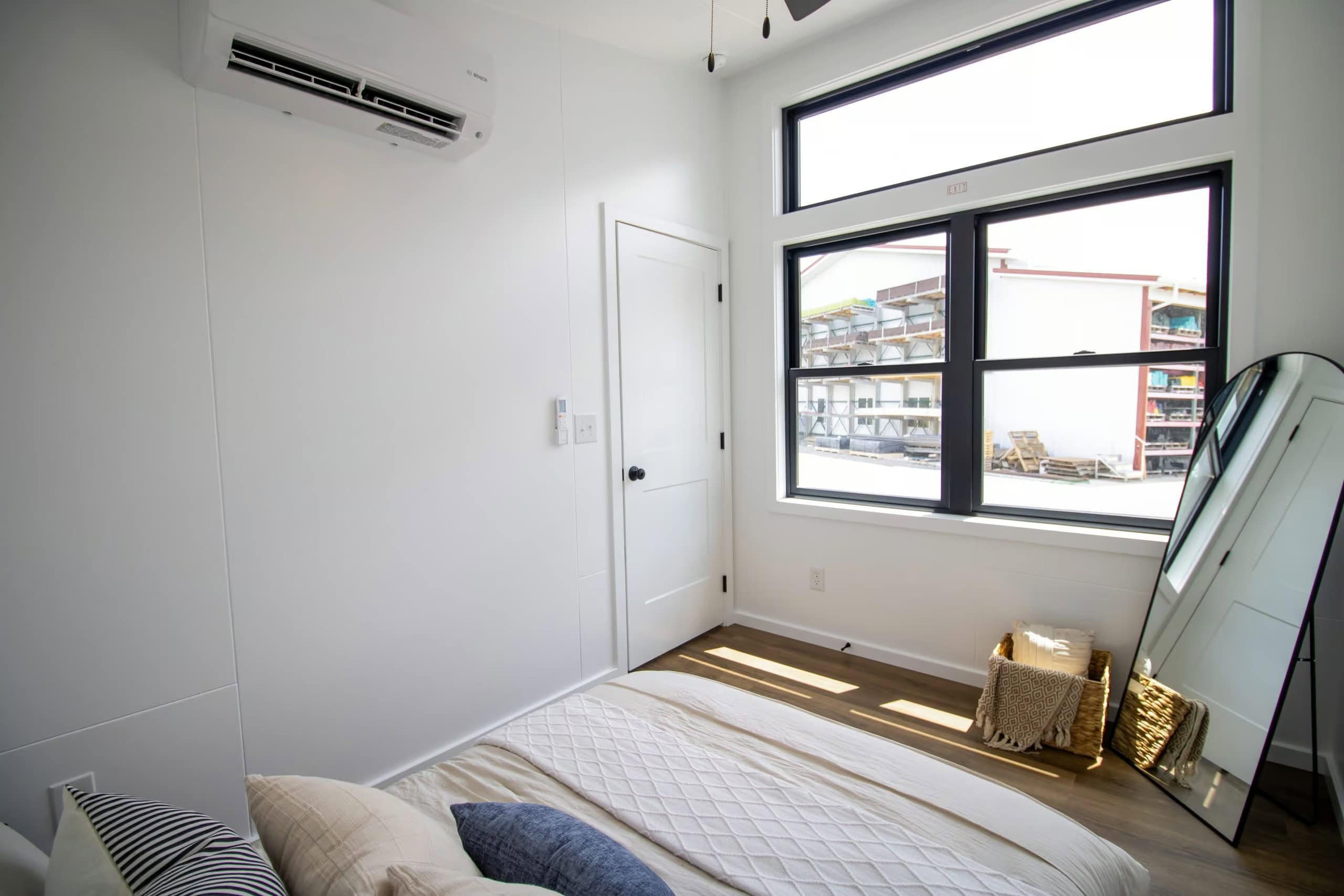 Bedroom window wall: two black-framed Anderson panes with a transom, leaning oval mirror, white two-panel door