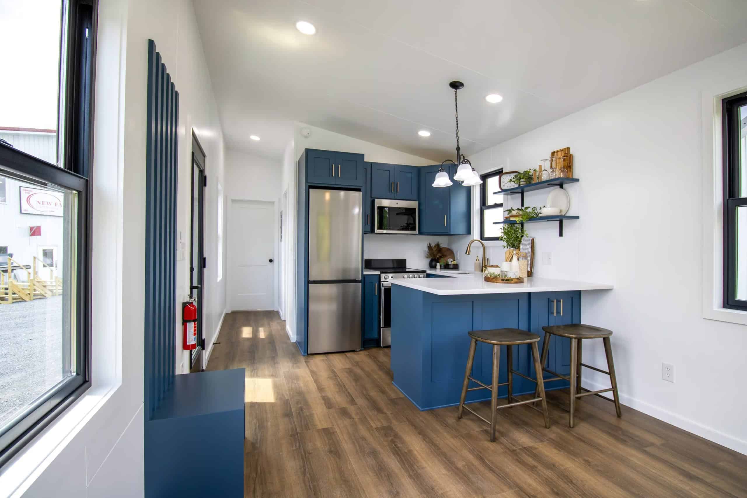 From the full-glass entry: navy built-in bench, navy kitchen with stainless appliances, short white hall to a two-panel bedroom door