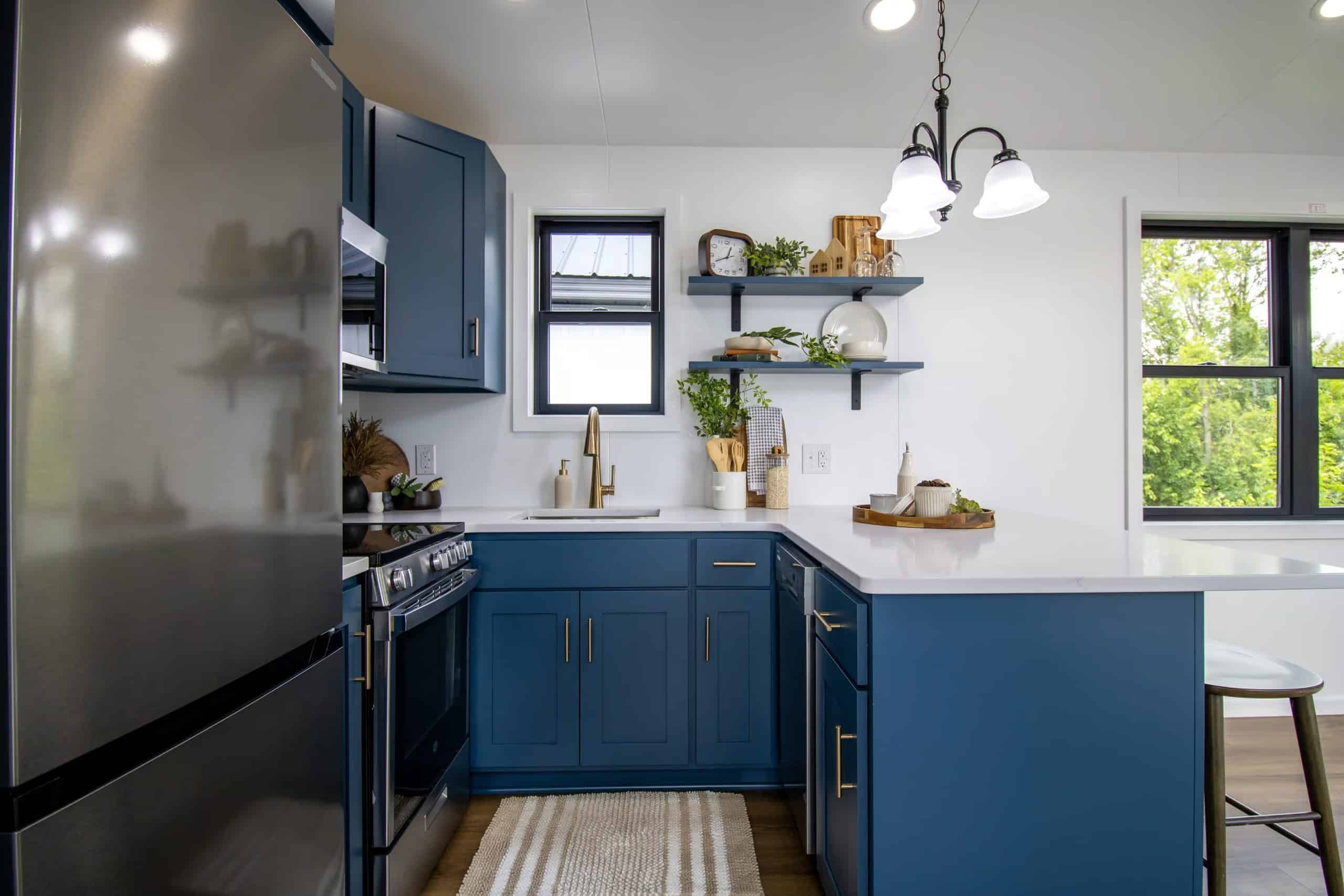 Navy kitchen with white quartz, stainless fridge, 30-inch electric oven and microwave, champagne faucet under a black-framed window