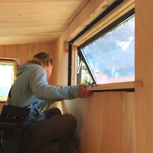 A student fits a wooden windowsill inside a Hammerstone tiny house