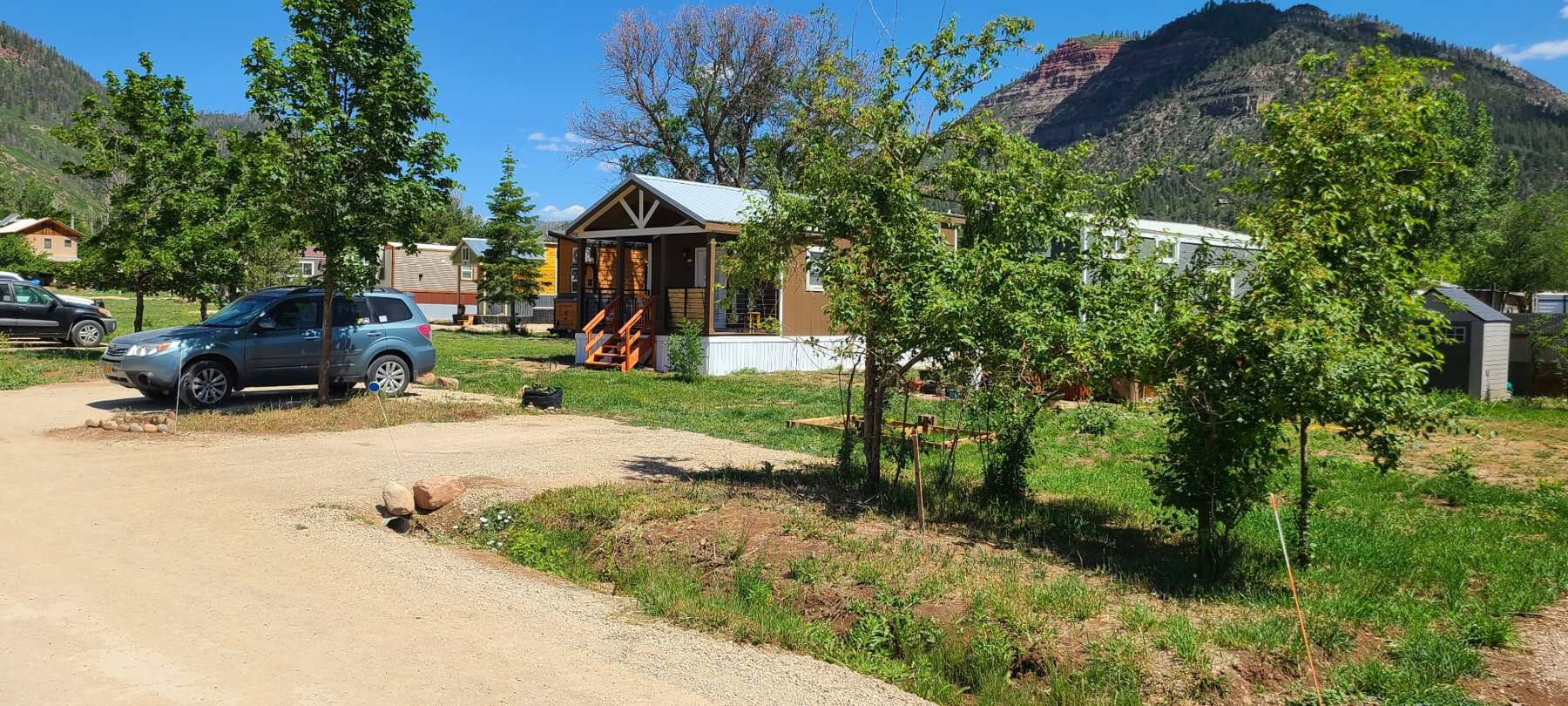 Tiny homes among trees with red-rock mountains behind at Hermosa Orchards Village
