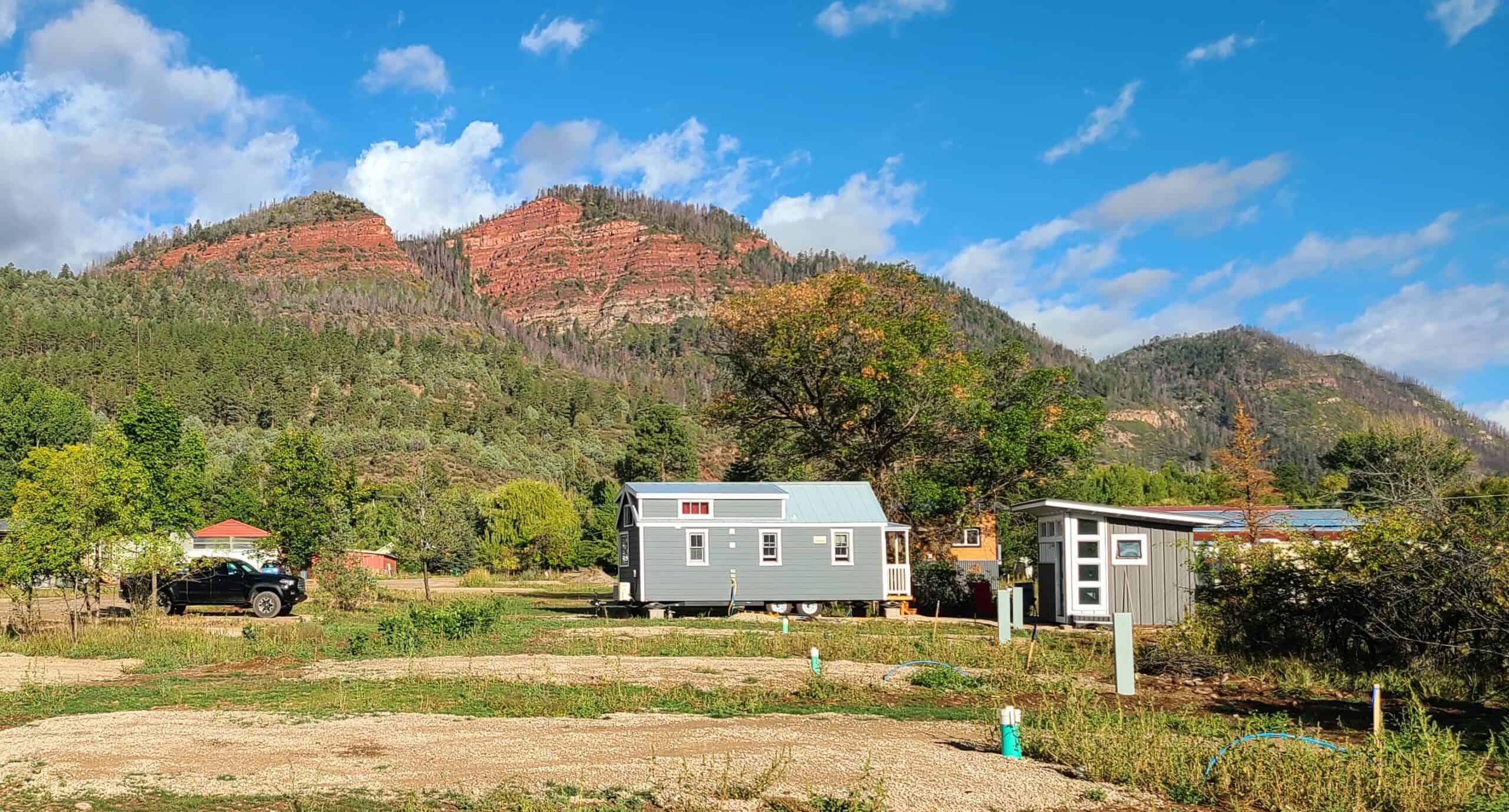 Pad with utility hookups visible, a grey tiny house and shed-style unit with mountain view at Hermosa Orchards Village in Durango