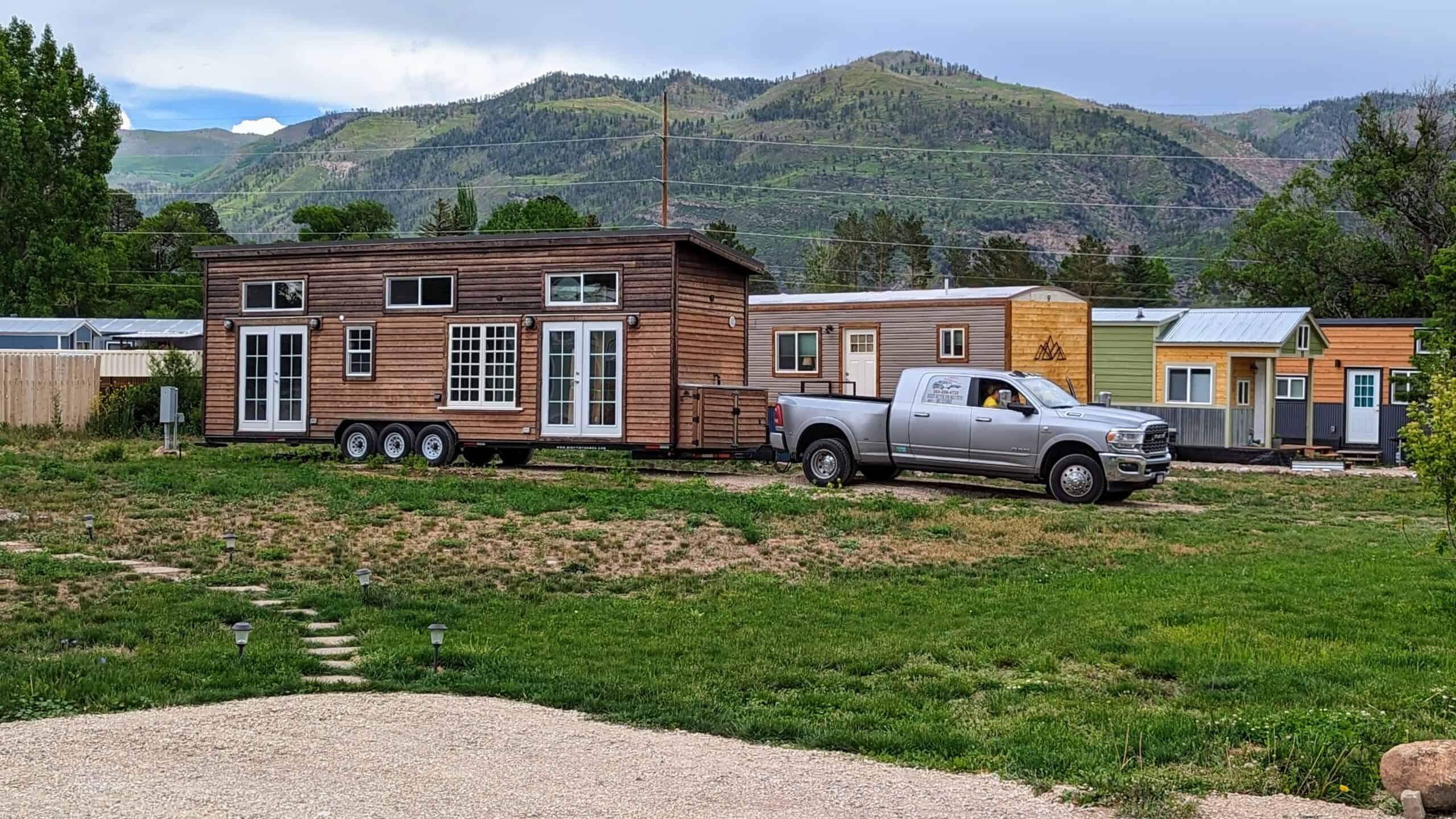 Wood tiny house on wheels being towed or set among other homes with a mountain backdrop at Hermosa Orchards Village in Durango
