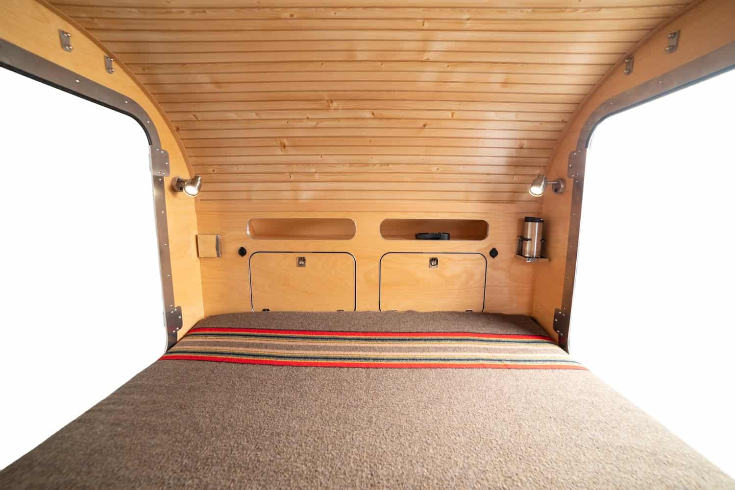 High Camp teardrop cabin with a queen mattress, striped blanket, and wood-paneled walls and ceiling