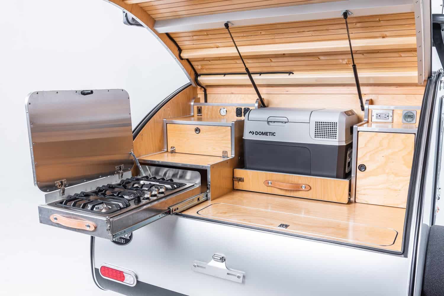 Stainless three-burner cooktop sliding out of the High Camp galley with its lid raised