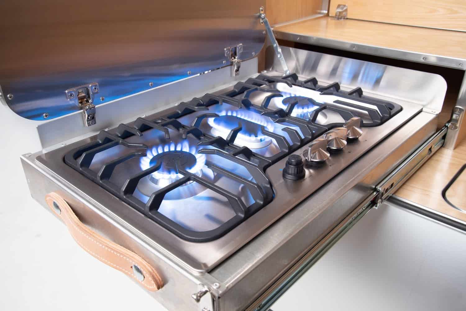 Close-up of the High Camp three-burner stove with blue flames and cast iron grates