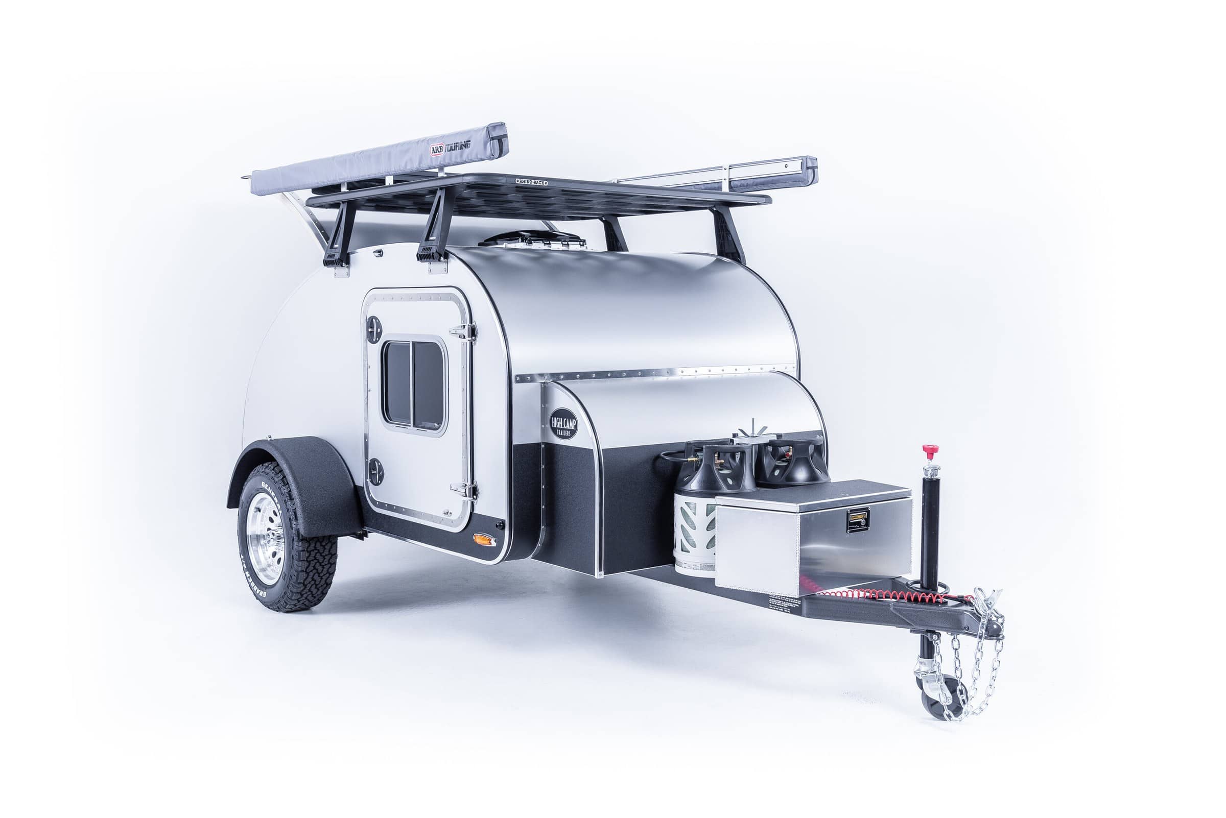 Three-quarter view of High Camp teardrop showing side door window, fender, and dual propane tanks on tongue