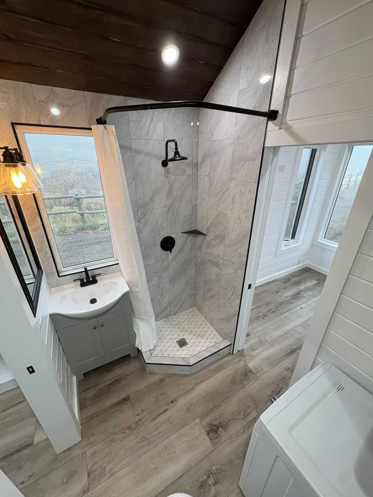 Tiled bathroom with glass corner shower and laundry in the custom tiny house