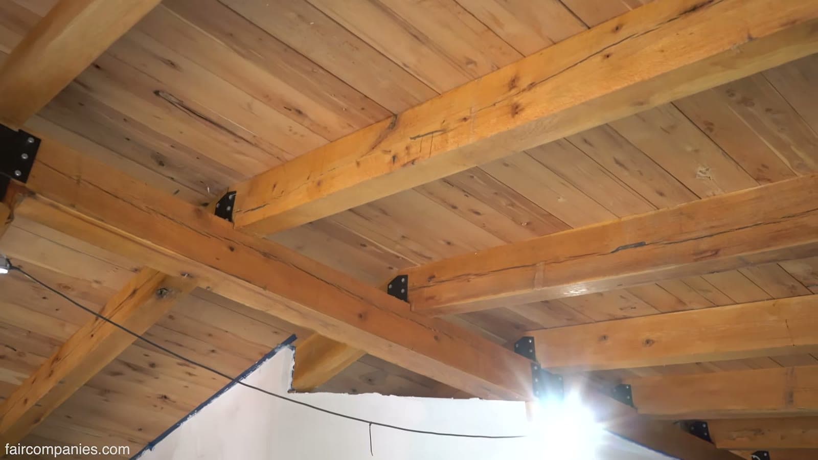 Looking up at heavy rough-sawn timber beams joined with black steel brackets under a board ceiling