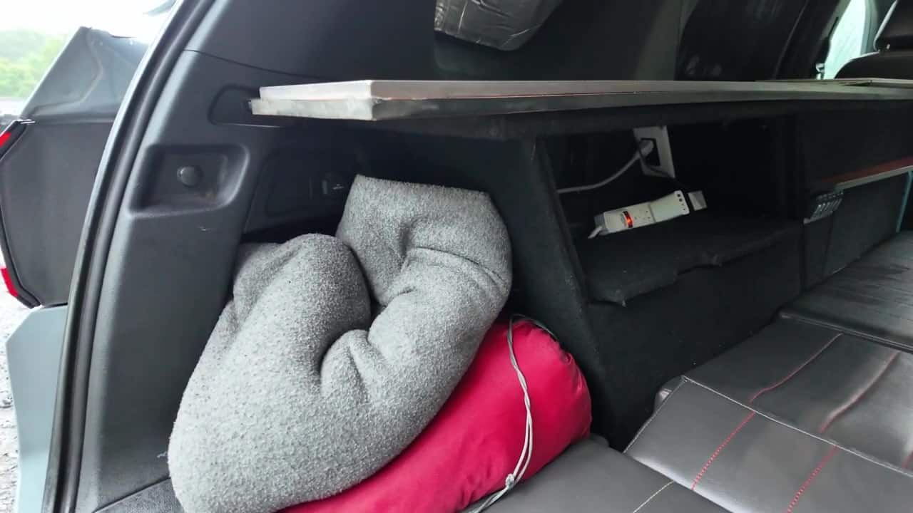 Carpet-wrapped cabinet cubbies along the driver side of the Honda Pilot camper with storage compartments, mounted power strip, and bedding tucked in