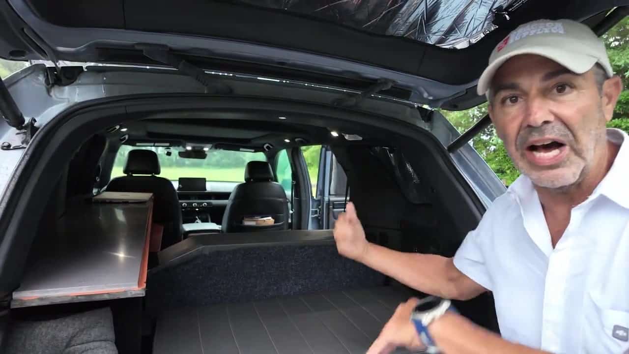 Rear-hatch view of the modular bed platform in Aaron's Honda Pilot with gray mattress, side desk, LED puck lights, and hatch-window blackout cover