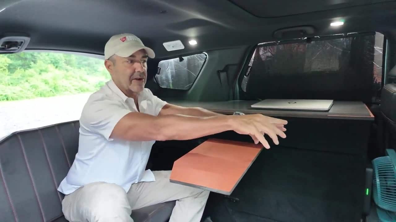 Custom sliding desk pulled out from the cabinet in Aaron's Honda Pilot camper with a laptop on the gray work surface and blackout covers behind