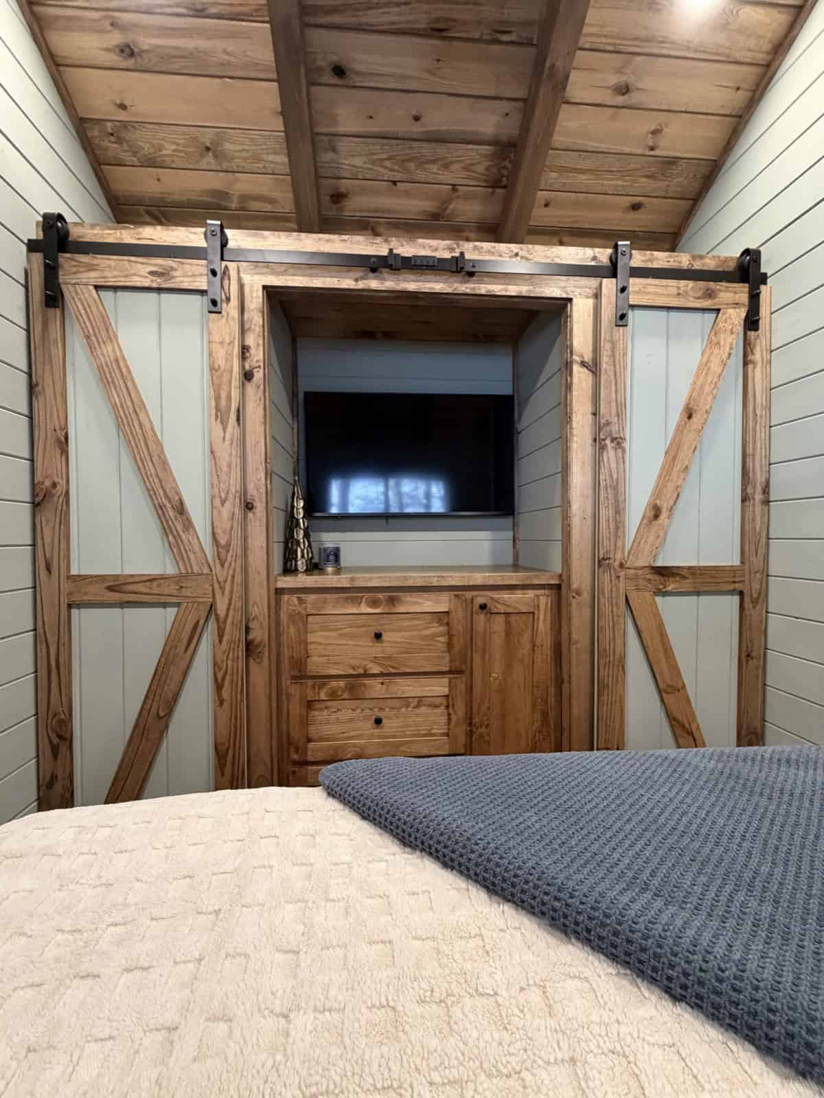 Sliding barn doors opening to a built-in TV cabinet with drawers at the foot of a tiny home bed
