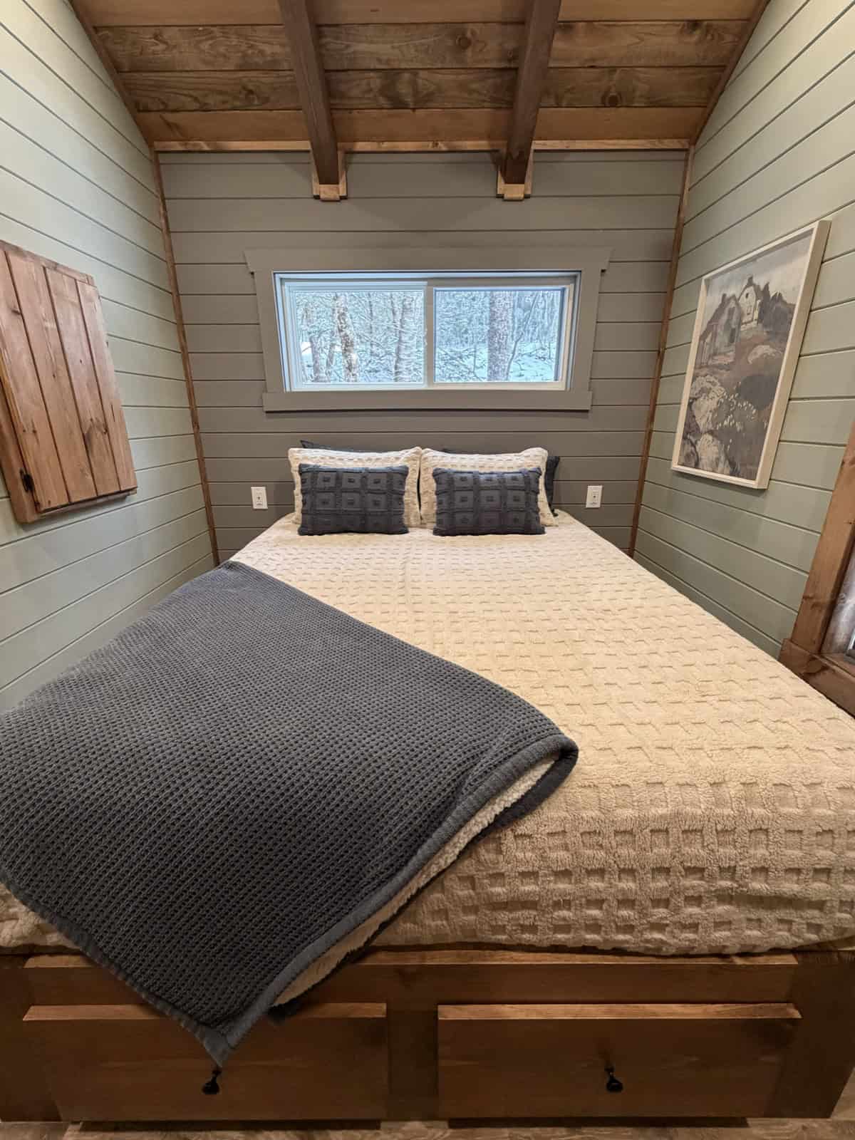 Tiny home bedroom with a queen bed on a wooden storage frame, shiplap walls, and a wood plank ceiling