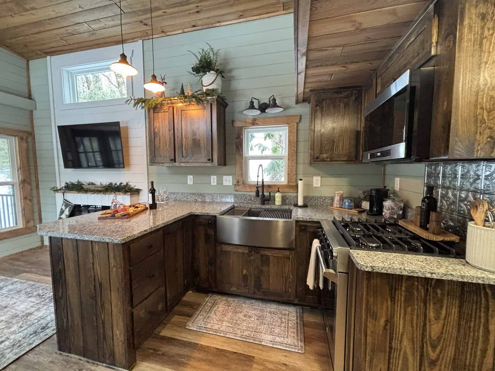 Rustic tiny home kitchen with dark wood cabinets, granite counters, a farmhouse apron sink, and a stainless gas range