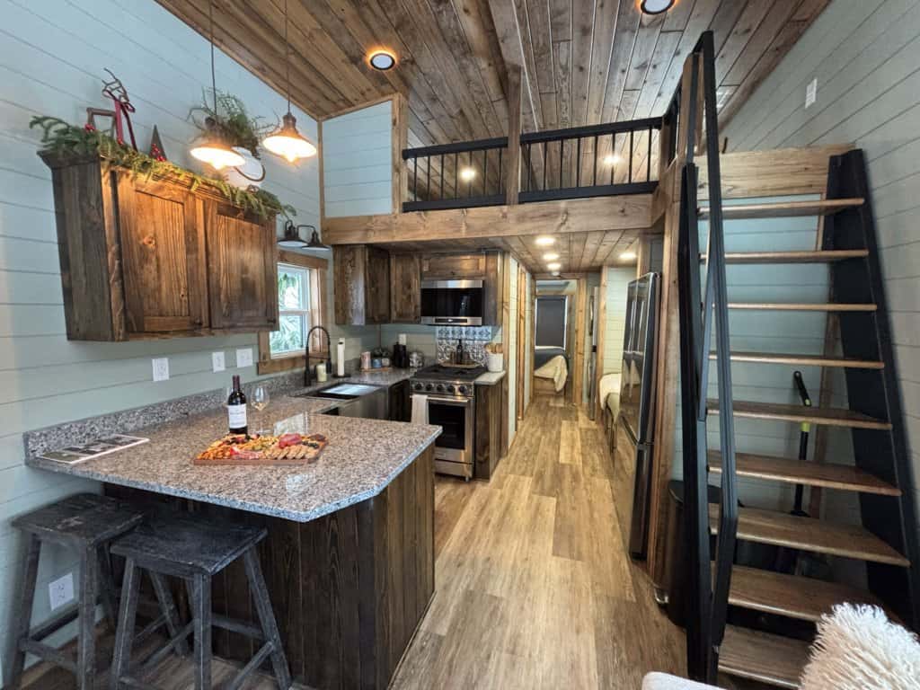 Sage shiplap kitchen with dark wood cabinets, breakfast bar stools, stainless range, and an open loft over the hallway