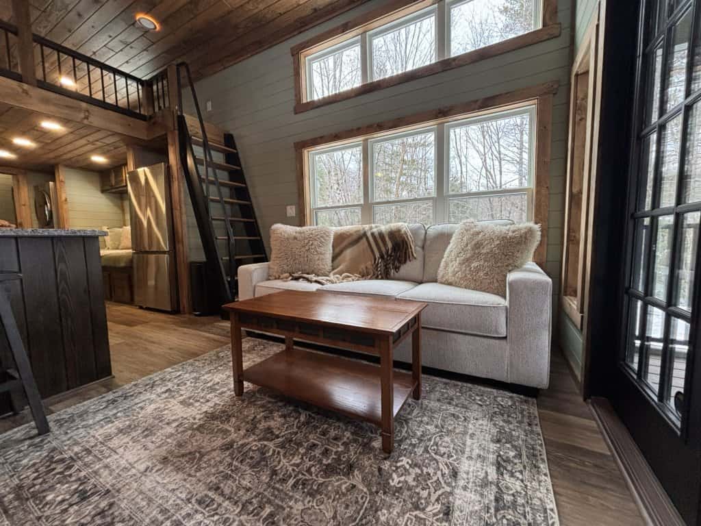 Sage shiplap living room with a light sofa under a three-pane window, black-rail stairs to a loft, and a glass door to the deck