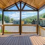Covered wooden porch with hog-wire rail looking out over gravel lots, neighboring tiny homes, and mountains
