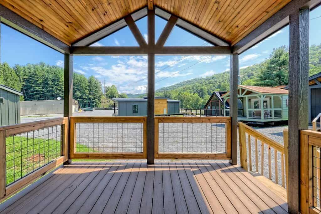 Covered wooden porch with hog-wire rail looking out over gravel lots, neighboring tiny homes, and mountains