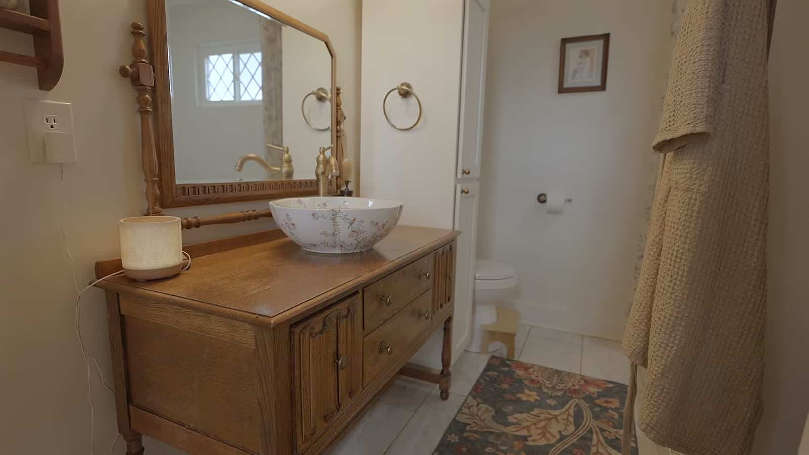 Bathroom vanity made from an antique wooden dresser with a white vessel sink, brass faucet and vintage mirror