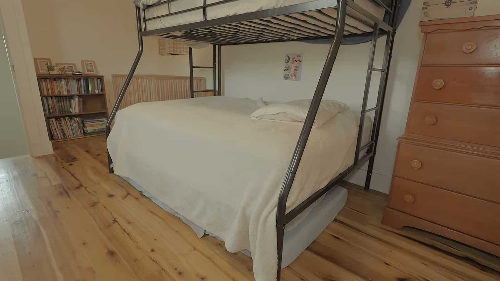 Upstairs kids' bedroom with black metal twin-over-full bunk bed, wooden dresser, bookcase and wood floors
