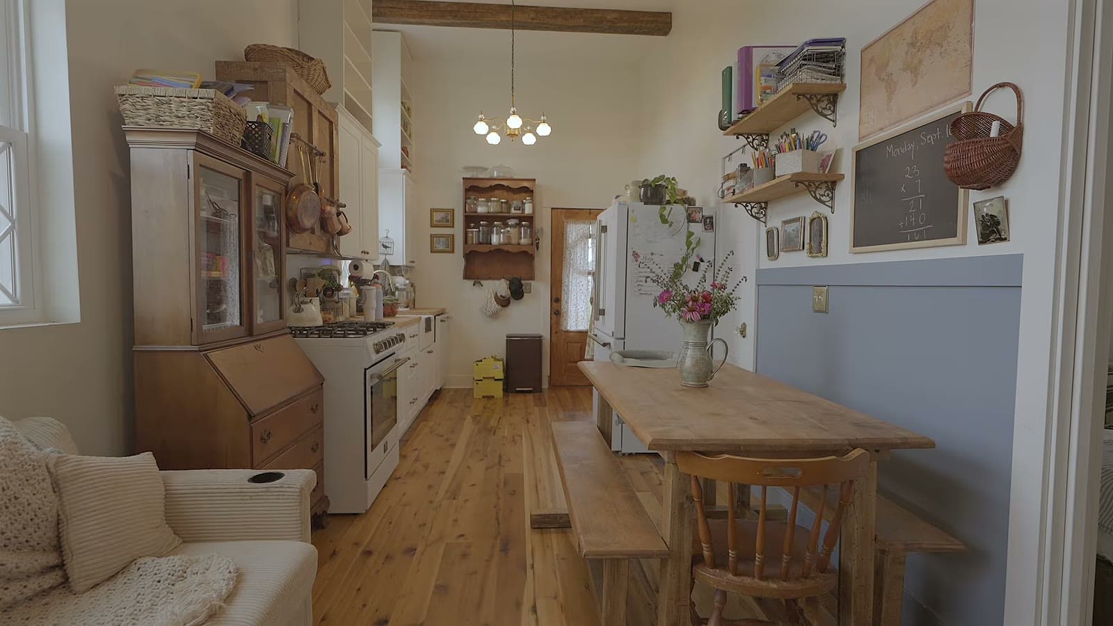 Long wooden dining table with bench and chairs between the kitchen and living room, with an antique hutch and open shelving
