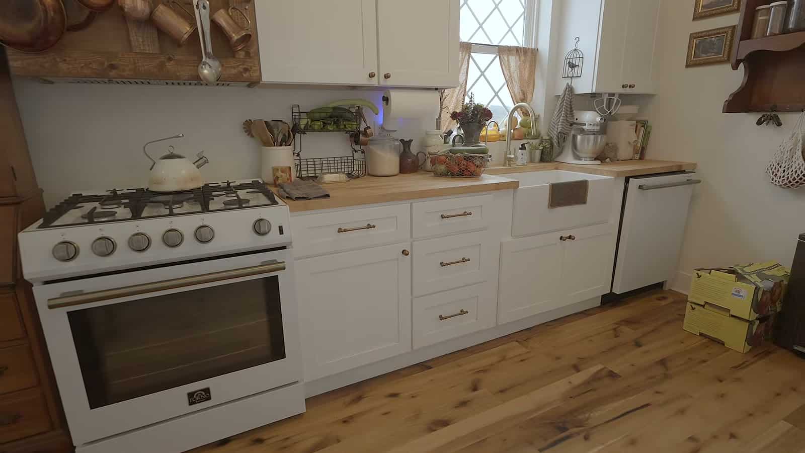 Farmhouse kitchen with white gas range, white shaker cabinets, butcher block counters, farmhouse sink and dishwasher
