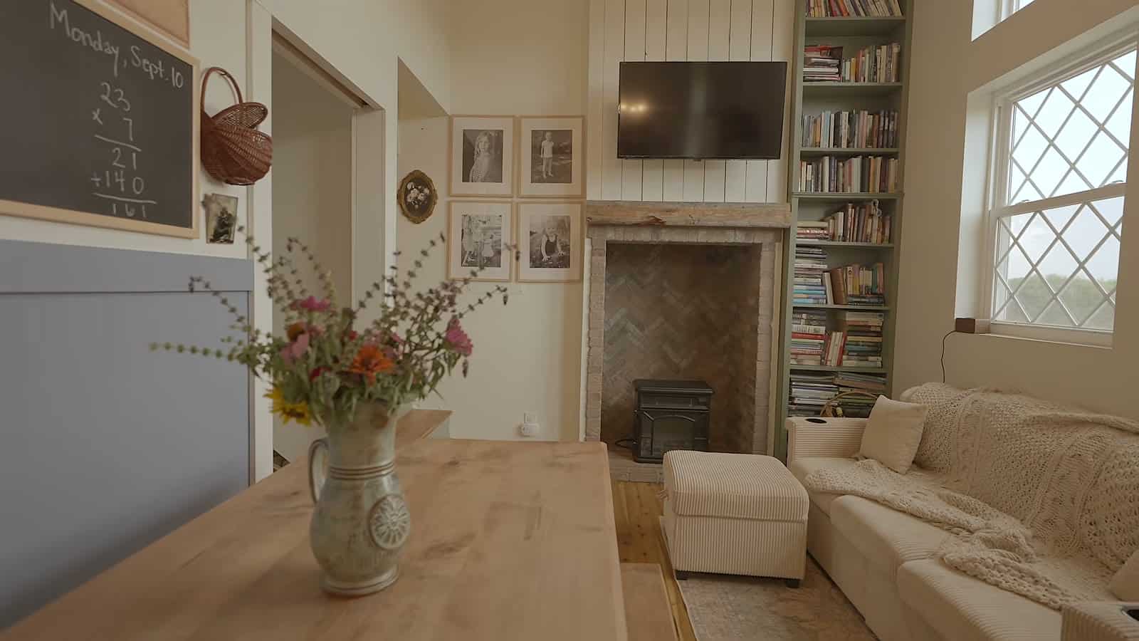 Tiny farmhouse living room with brick fireplace and stove, timber mantel, built-in bookshelves, wall-mounted TV and diamond-pane windows