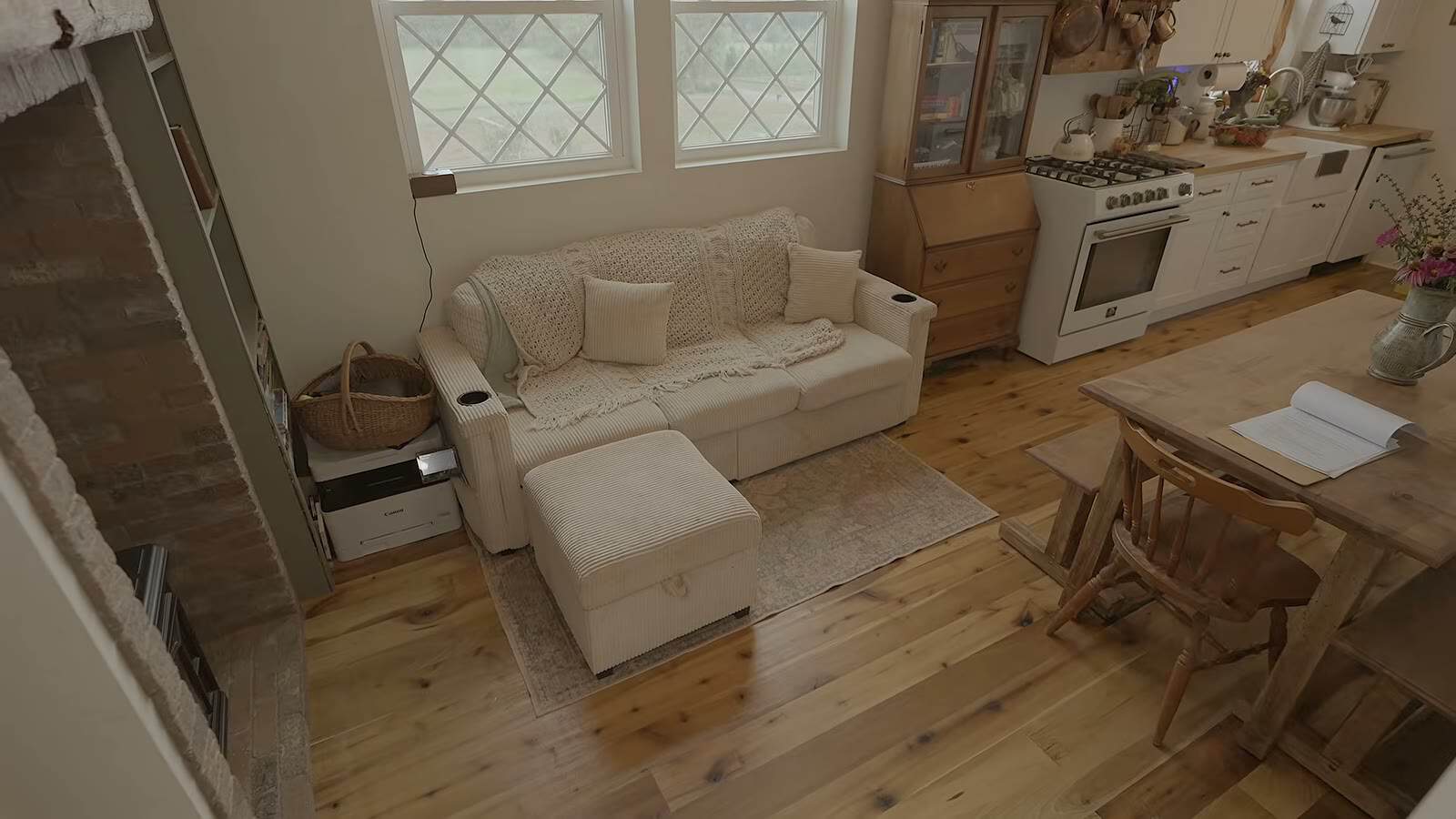 Cream sectional sofa and storage ottoman under diamond-pane windows, with the kitchen and range in the background