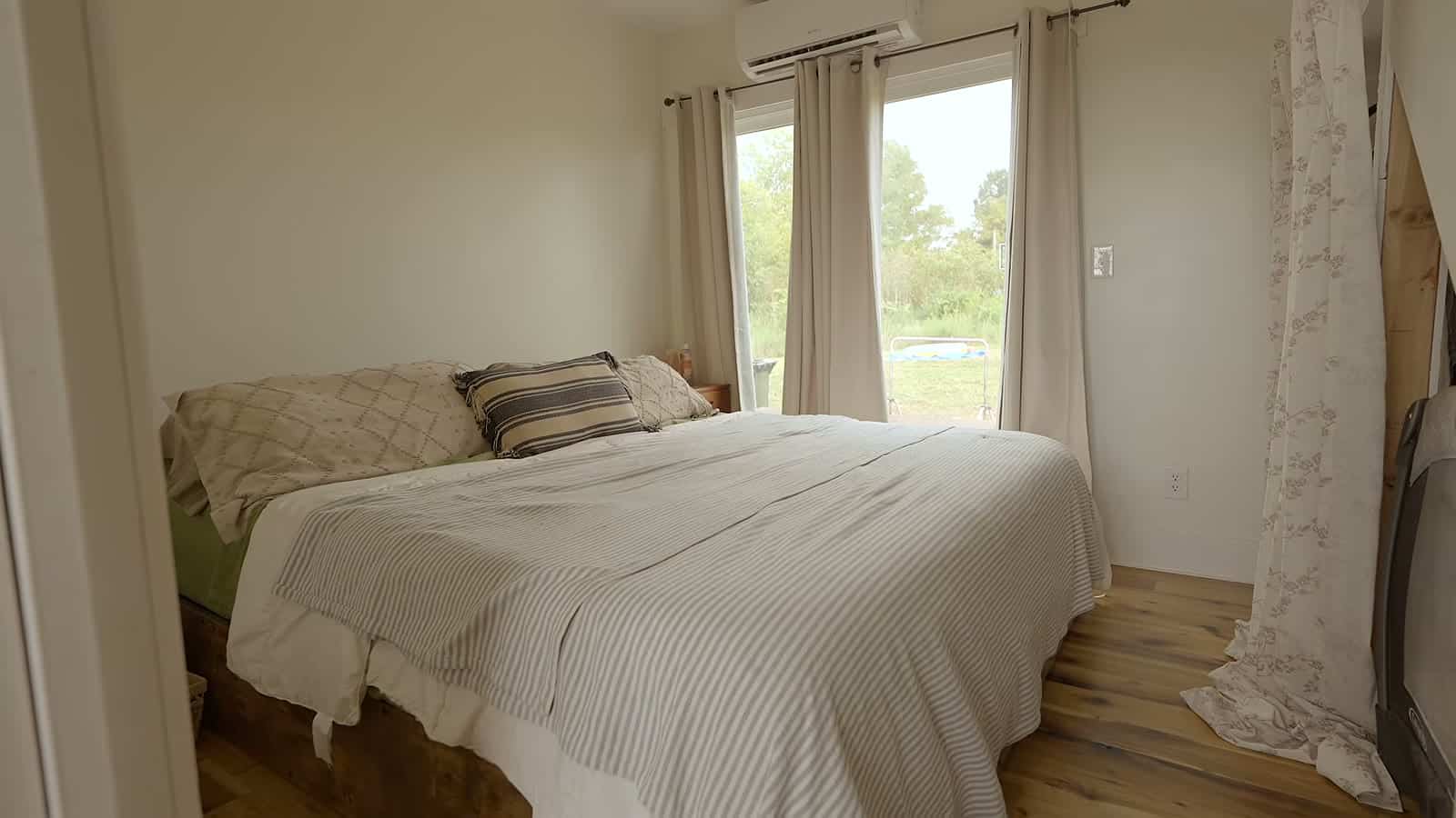 Main floor bedroom with queen bed, striped pillows, curtained window and fabric-curtained closet under the stairs