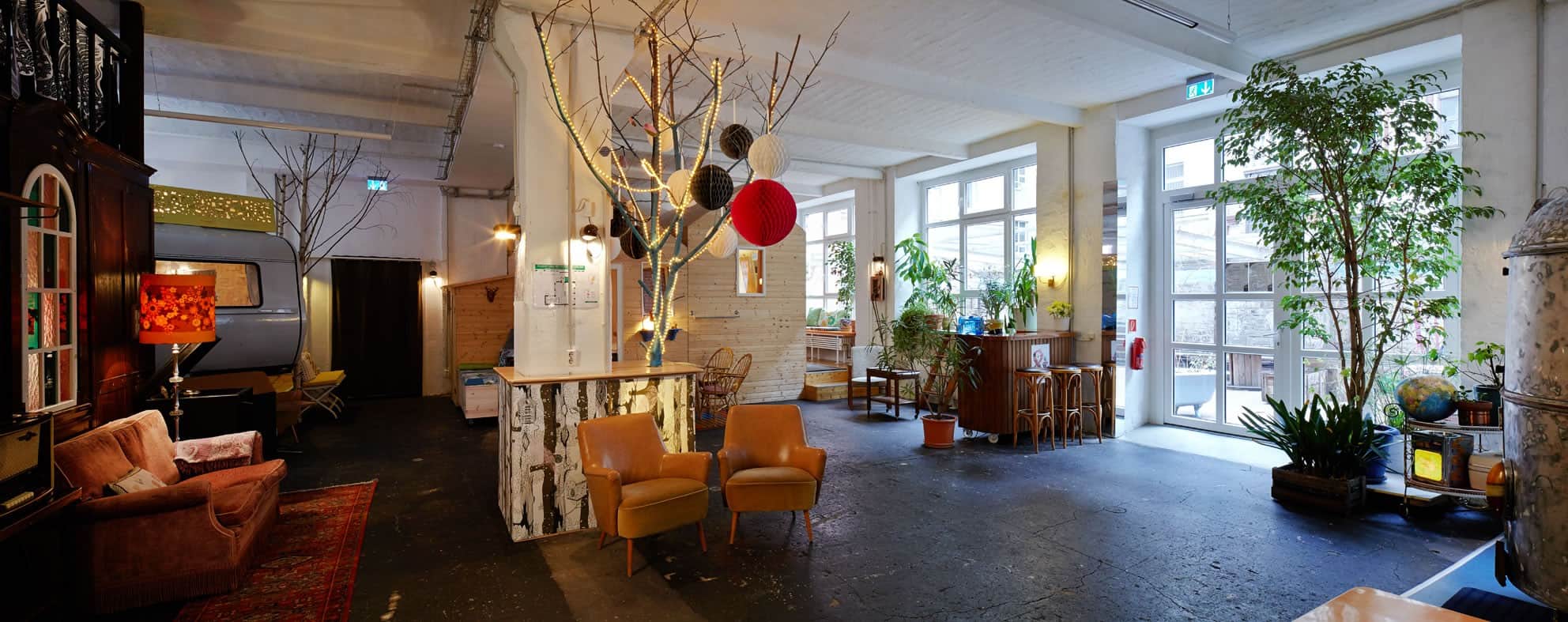Hall 1 factory common: vintage caravan, wooden hut, retro lounge and plants in a former factory hall
