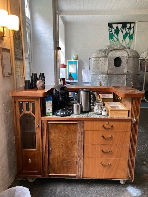 Self-service coffee and tea station on a vintage wooden cabinet, kettle and mugs, caravan behind