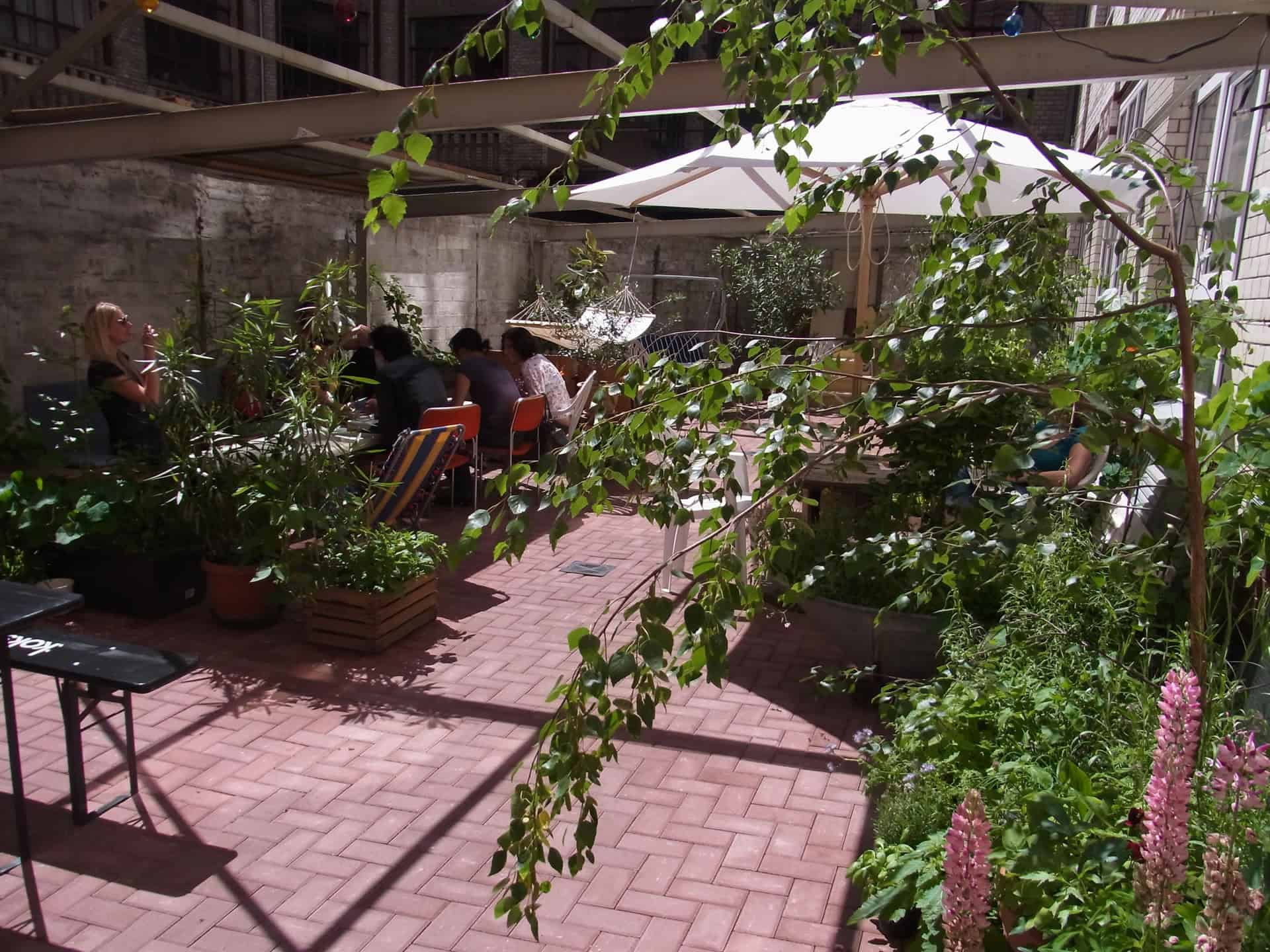 Brick courtyard garden with plants, string lights, and seating beside the factory wall